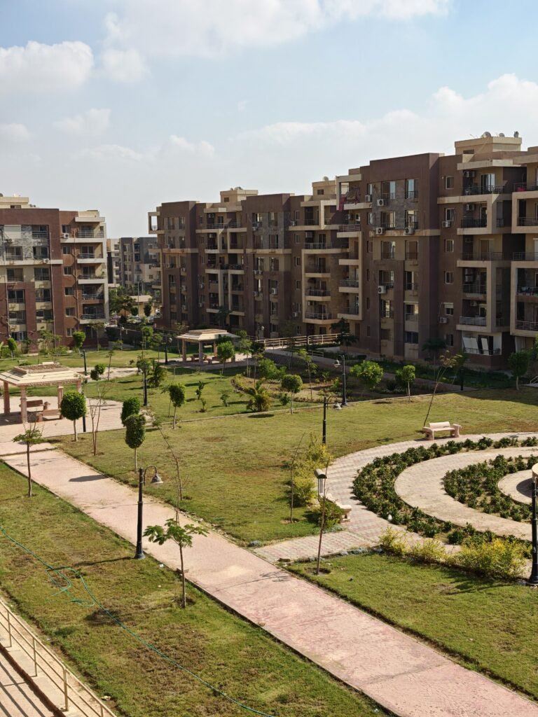 Aerial view of a modern apartment complex with landscaped gardens and pathways under a clear sky.